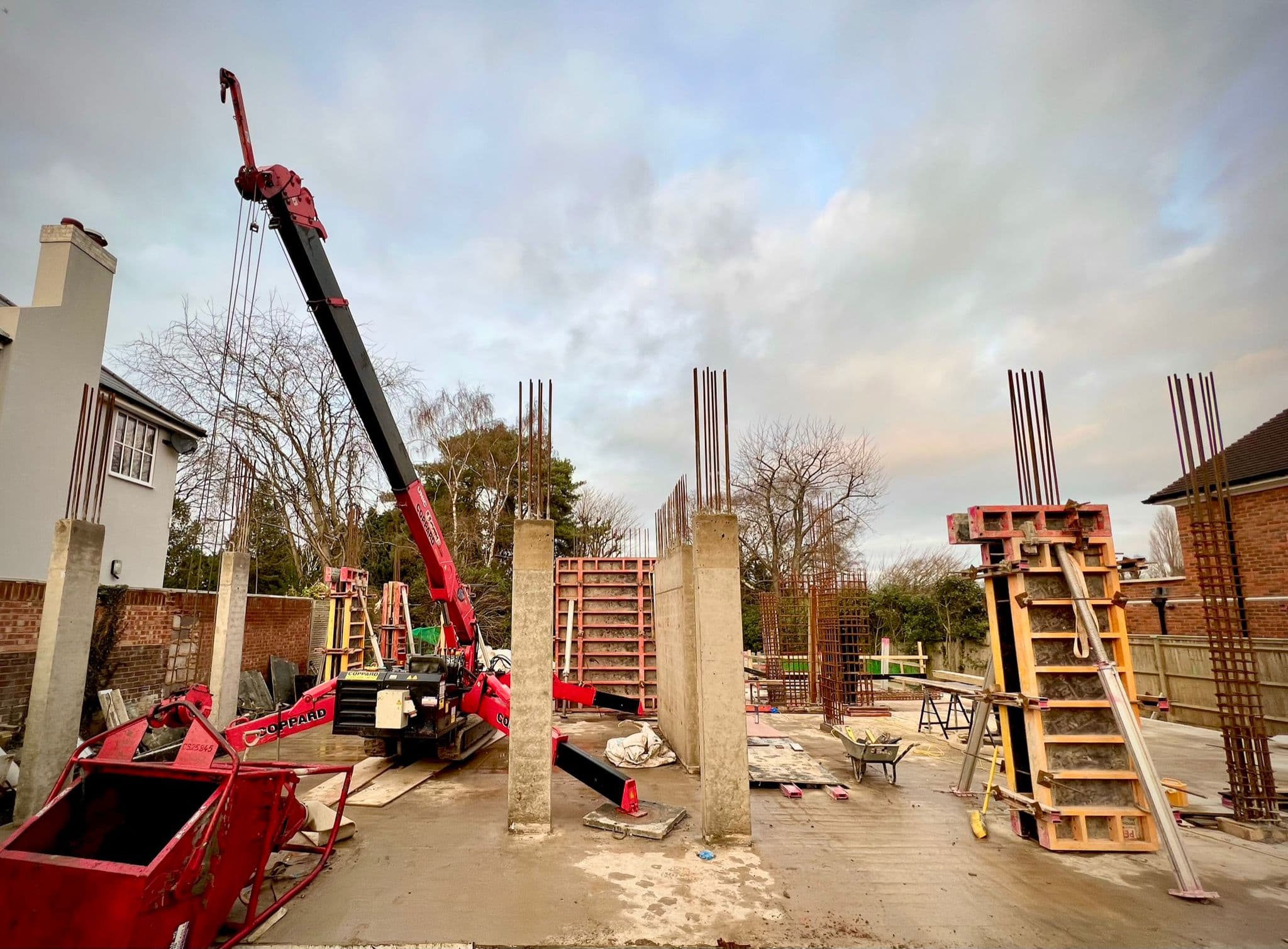 Red crane lifting steel reinforcement with cast concrete columns and formwork on site